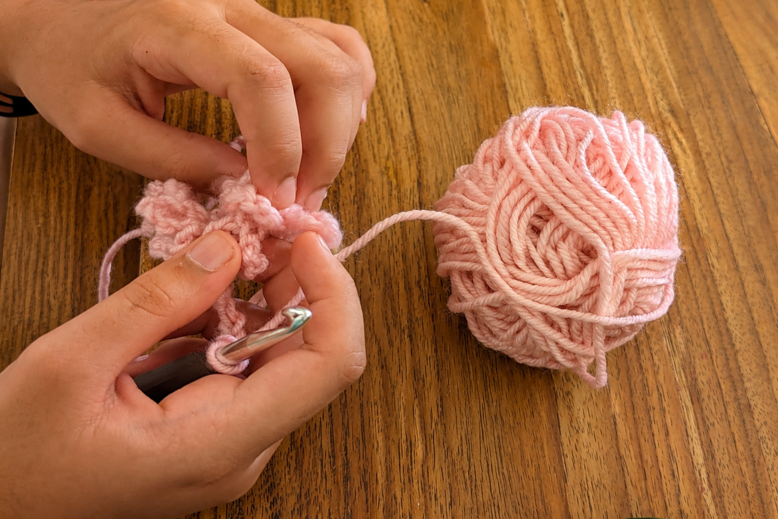 Hands learning an early crochet stitch with pink yarn